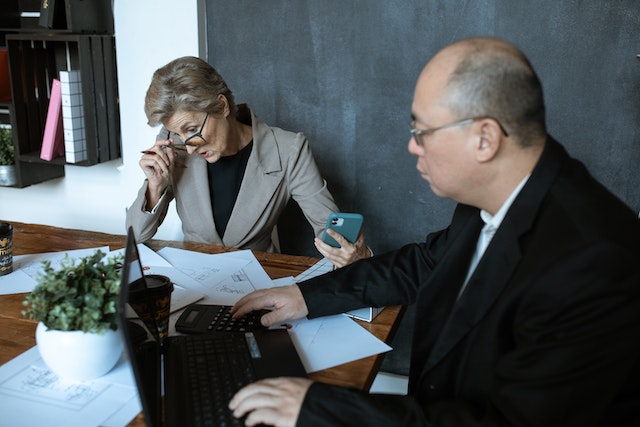 two people sitting at a desk looking over budgets with a calculator between them